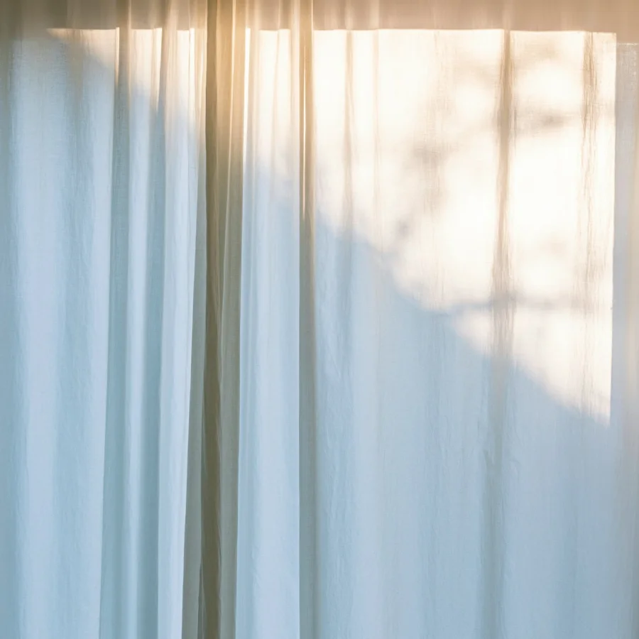 Sunlight and the shadow of a tree falling on a sheer linen curtain.